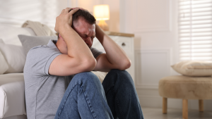 Mann sitzt verzweifelt am Boden und schlägt die Hände über dem Kopf zusammen – Sinnbild für Panikattacken und mentale Überforderung.