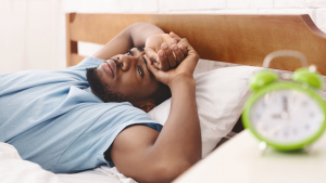 Mann liegt nachts wach im Bett; Schlaflosigkeit verhindert Muskelaufbau und Regeneration.