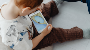 Kleinkind sitzt auf dem Boden und schaut auf ein Smartphone – Bildschirmzeit bei Kindern